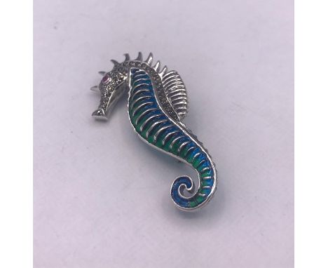 A silver and enamel sea horse shaped brooch with ruby eye