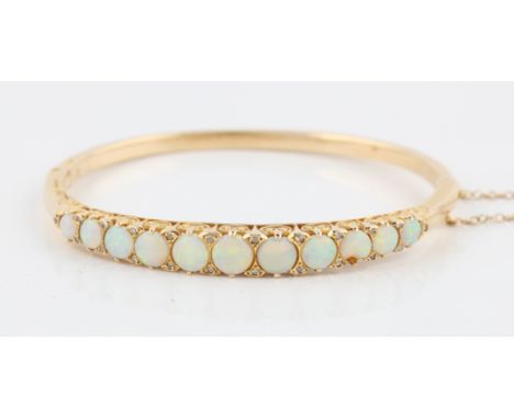 A late 20th Century Edwardian style 14ct yellow gold opal hinged bangle, set with eleven graduated round opal cabochons, inte