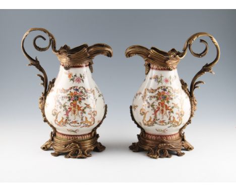 A pair of 20th Century ceramic jugs with cherub and floral design bodies with bronzed scroll design mounts and handles.