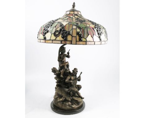 A table lamp, with Tiffany style leaded glass shade, decorated with grapes and leaves, the metal base sculpted with two figur