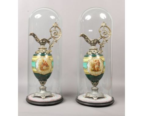 A pair of early 20th century Vienna style ceramic urns with metal mounts under large glass domes, height 73cm, diameter 32cm 
