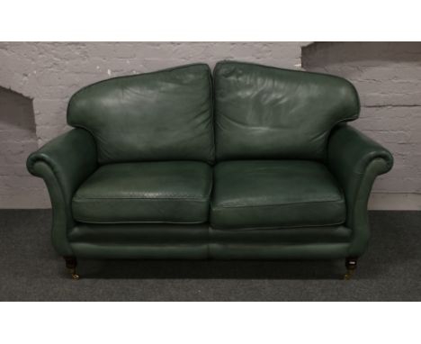 A green leather three seat sofa raised on brass castered turned mahogany legs.