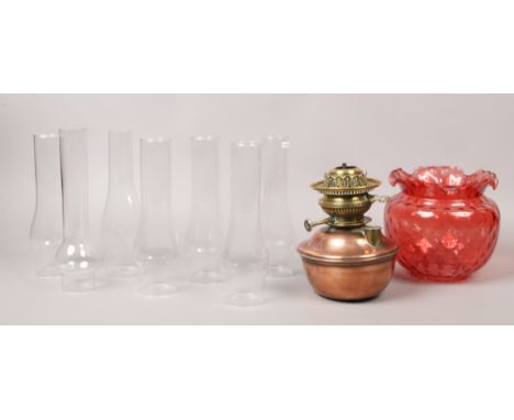 A copper and brass oil lamp font, along with a cranberry coloured glass shade and seven glass chimneys.