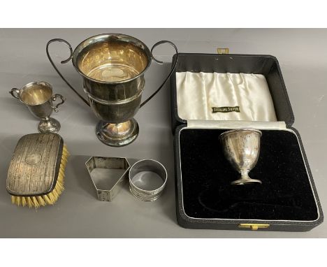 Cased silver egg cup, 2 small silver trophies, 2 silver napkin rings &amp; a silver backed hair brush. Weight of silver exclu