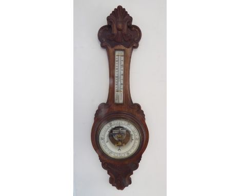 A late 19th century carved oak aneroid barometer; the cresting carved with central scallop-shell motif and flanked by C scrol