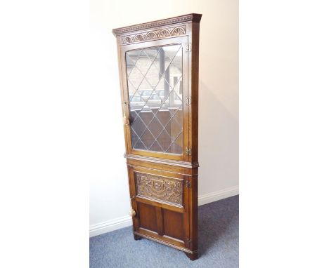 A freestanding reproduction oak corner cupboard; the cornice above a frieze carved with lunettes and a glazed leaded-light do