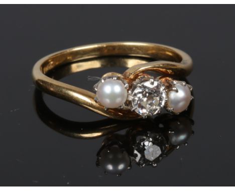 An antique 18 carat gold diamond and pearl crossover ring. With a central round cut diamond approximately 0.4ct flanked by tw