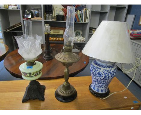 Two Victorian oil lamps, one with a cast iron base, a floral enamelled opaline reservoir and etched glass shade, along with a