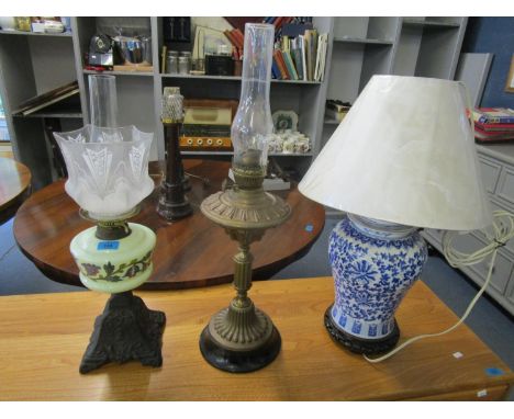 Two Victorian oil lamps, one with a cast iron base, a floral enamelled opaline reservoir and etched glass shade, along with a