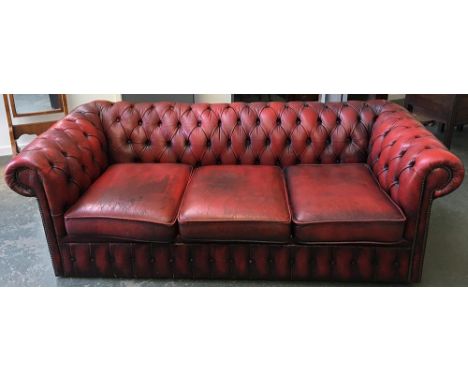 A three seater button back Chesterfield sofa upholstered in oxblood leather 