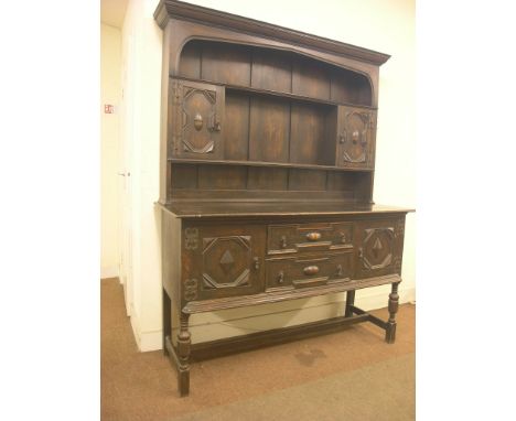 An early 20th century solid, dark oak dresser, twin-shelf plate rack with spice cupboards, panelled cupboard base with two dr