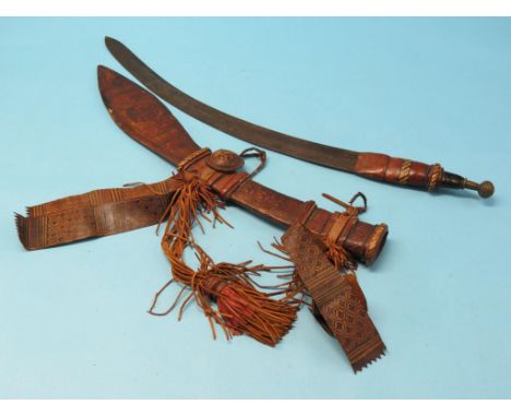 An African mandingo sword, 24in. curved, single-edged blade, hilt with brass pommel, within embellished tooled leather scabba