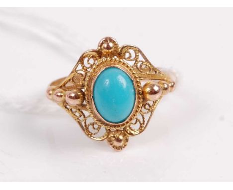 A yellow metal turquoise set dress ring, the cabochon turquoise in a pierced scroll work surround, unmarked, tests as approx 