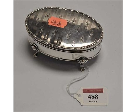 An Edwardian silver trinket box, of oval form, having hinged cover with engine turned and floral decoration, with lined inter