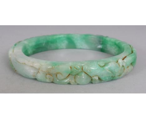 A LARGE CHINESE APPLE GREEN JADE BANGLE, the outer rim carved with lingzhi, carp, lotus, finger citron and other motifs, 4.25