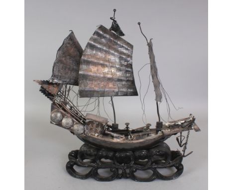AN EARLY 20TH CENTURY CHINESE SILVER-METAL MODEL OF A JUNK, supported on a fixed & pierced lacquered wood stand, the stern of
