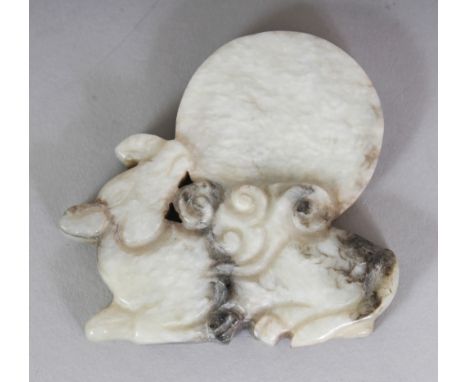 A CHINESE MING STYLE JADE MODEL OF A RECUMBENT KYLIN, bearing a disc upon its back, the pale stone with some dark inclusions,