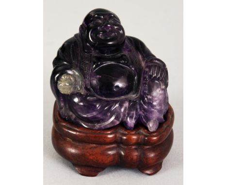 A SMALL CHINESE AMETHYST MODEL OF A SEATED BUDAI, together with a fitted wood stand, 2.25in high overall, the carving itself 