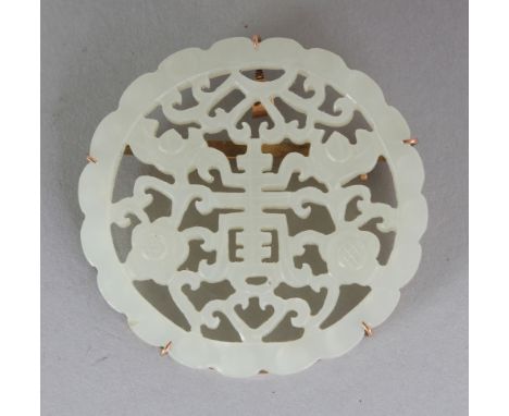 A CHINESE GOLD MOUNTED CIRCULAR PIERCED JADE PLAQUE, the jade carved with flowerheads and lotus, the brooch mount with a 'K 1