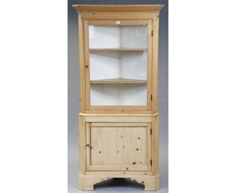 A pine tall standing corner cabinet the upper part fitted two shelves enclosed by a glazed door, the base fitted shelf enclos
