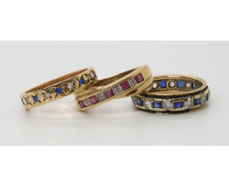 Three gem set eternity rings, a ruby and diamond, size N, a blue and clear gem, size N1/2, together with a blue and clear gem