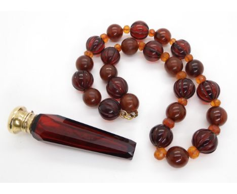 A string of mixed amber coloured beads weight 104gms, together with a ruby glass scent bottle with gold plated cap Condition 