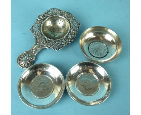 A Continental white metal tea strainer with pierced foliate border and handle, 14cm long and three white metal dishes set wit