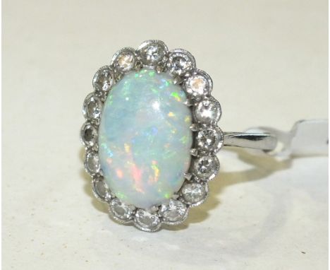 An opal and diamond cluster ring, claw set an oval opal of 13 x 9.5mm within a surround of sixteen brilliant cut diamonds, in