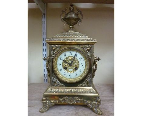 A Victorian brass mantle clock with cast detail, side handles and urn finial and enclosing and 8 day striking movement