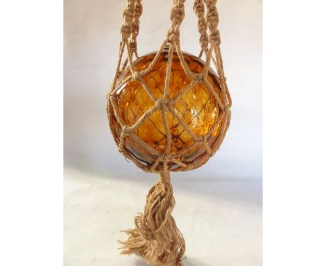 A large amber glass buoy converted to a lamp contained within woven hessian netting