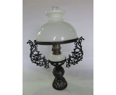 An oil lamp with opaque glass fount set within an elaborate pierced ironwork stand and frame with trailing garland, foliate a
