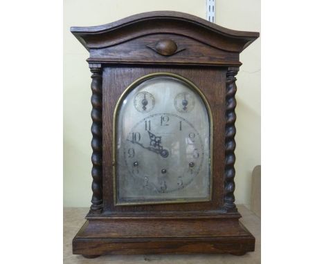 An Edwardian oak bracket clock with barley twist supports, the arched silvered dial with regulator and chime/silent selector 