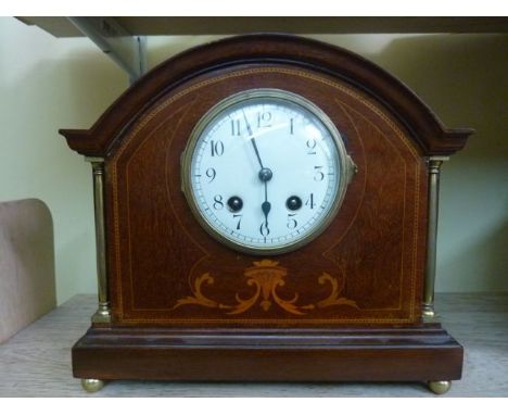 An inlaid Edwardian mahogany mantle clock with brass column supports and with eight day striking movement
