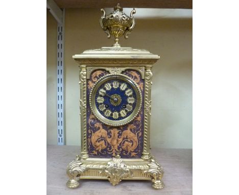 A brass cased mantle clock with cast detail set beneath an urn with eight day striking movement