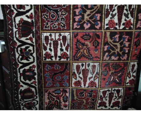 A Persian style wool carpet, the central field divided into a multitude of square panels with abstract floral decoration with