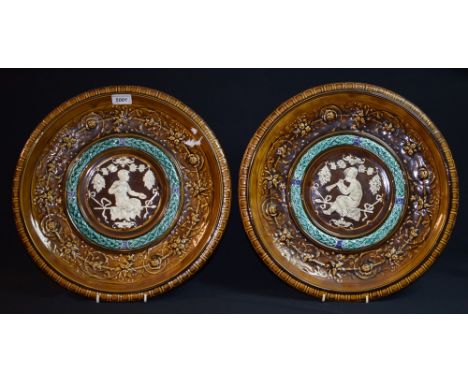 A pair of Clément Massier wall plaque chargers, relief decorated with a central figure of satyr upon a ribbon bench, double l