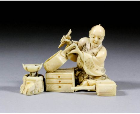 A Japanese carved ivory okimono of a carpenter seated by a small chest of three drawers, a tool in his right hand, a box in h