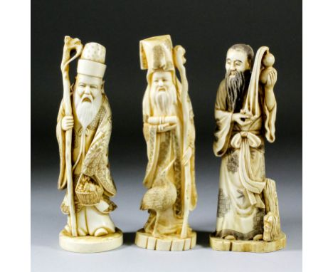 Two Chinese carved ivory standing figures of bearded sages, each holding a staff, one holding a basket of fruit with a rat pe