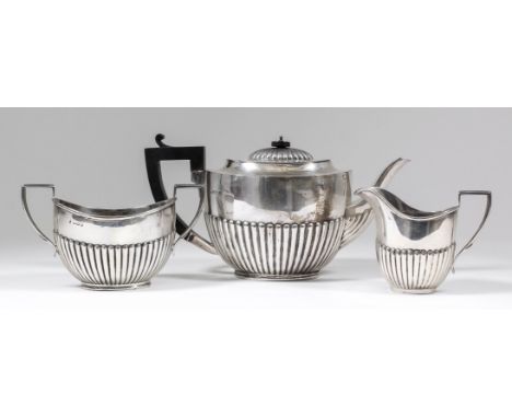 A George V silver three piece tea service of Georgian design, with oval partly reeded bodies comprising - teapot with ebonise