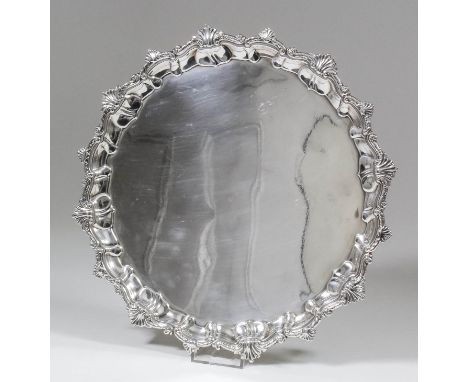 A George V silver circular salver, the shaped and moulded rim cast with shell and scroll ornament and on four leaf capped scr
