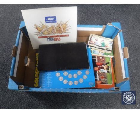 A box containing humorous postcards, Esso 1970 World Cup coin collection, Shell Great Britain coin collection, football books