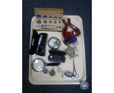 A tray containing set of cased weights, magnifying glass, vintage spectacles, glass eye bath, fob watch case, rabbit's foot b