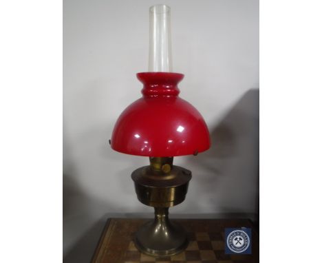 A brass Aladdin oil lamp with chimney and red glass shade