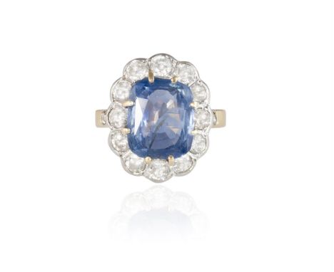 A SAPPHIRE AND DIAMOND CLUSTER RING, CIRCA 1920The cushion-shaped sapphire, weighing approximately 5.50cts, within a transiti