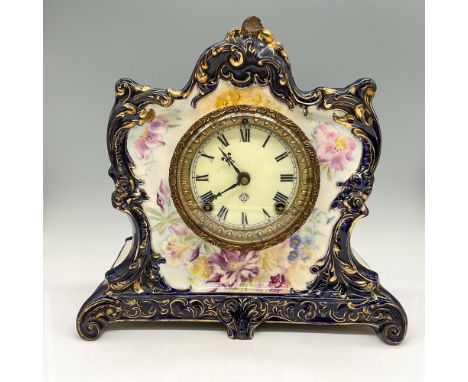 Clock porcelain body colored in royal blue with gilt highlights and floral motif around face of clock. Roman numerals on meta