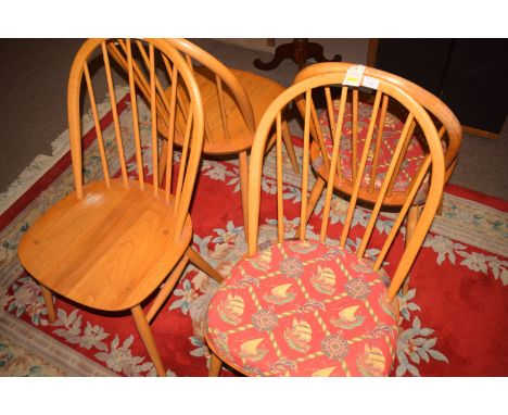 Four beech wood and elm seated Ercol dining chairs (some damages).