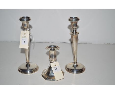 A pair of silver candlesticks with urn-shaped sconces and tapering stems; together with another candlestick of octagonal form