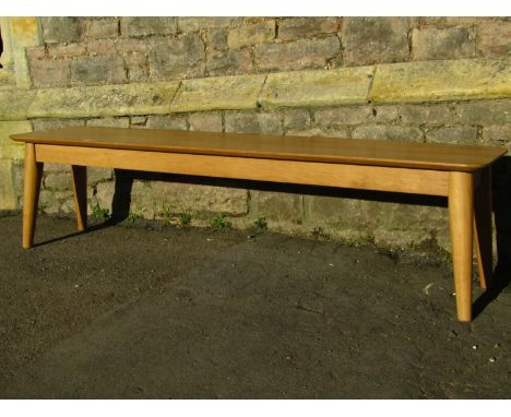 A contemporary light oak low long occasional table/bench of rectangular form with moulded outline raised on turned tapered su