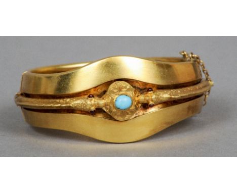 A Victorian unmarked 15 ct gold bracelet
Of hinged bangle form, decorated with twin garnet eyed serpents flanking the cabocho