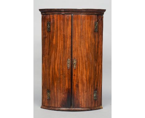 A George III mahogany bow front corner cupboard
The moulded cornice above twin doors with ornate brass escutcheons, enclosing